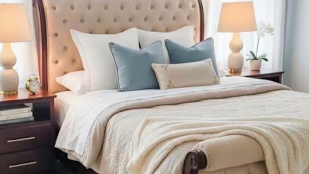 Een bed met een gestuufd hoofdeinde, een nachtkastje met een lamp en een nachttafeltje met een klok.