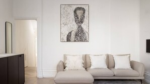 Ein Wohnzimmer mit einer Couch, einem Gemälde und einem Fernseher an der Wand.