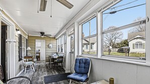 A room with a ceiling fan, a window with a view of houses, a chair, a table, and a rug. - Charming 6BR Colonial Beach Retreat, Walk to the Beach (Colonial Beach)