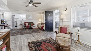 A spacious living room with a ceiling fan, a dark door, and a view through a window with blinds. - Charming 6BR Colonial Beach Retreat, Walk to the Beach (Colonial Beach)