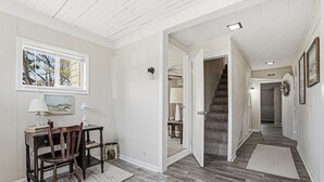 A hallway with a staircase, a desk with a chair, a lamp, and a painting on the wall. - Charming 6BR Colonial Beach Retreat, Walk to the Beach (Colonial Beach)