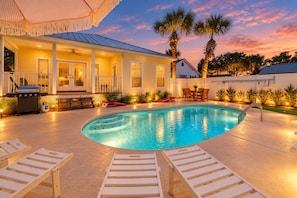 A swimming pool with lounge chairs, a barbecue area, and a covered patio with a view of the sunset. - Solstice-Free Golf Cart-Pool Heat Deals (Destin)