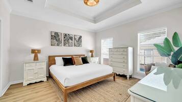 A bedroom with a wooden bed, white nightstands, a dresser, and a large window with blinds.