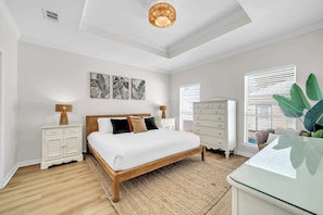 A bedroom with a wooden bed, white nightstands, a dresser, and a large window with blinds. - Solstice-Free Golf Cart-Pool Heat Deals (Destin)