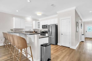 Une cuisine moderne avec des meubles blancs, des appareils en acier inoxydable, un coin bar avec des chaises en osier et un plancher en bois franc.
