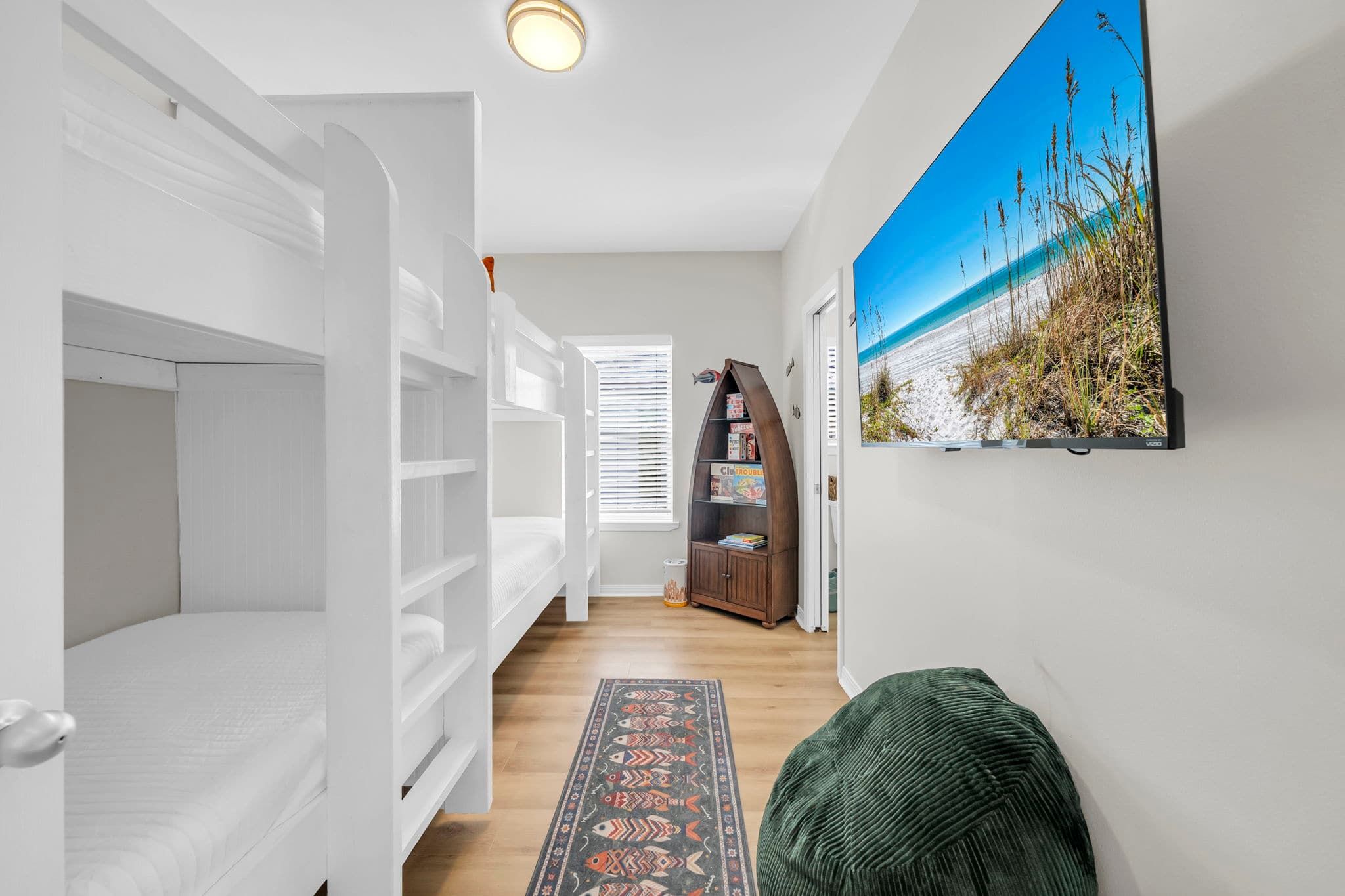 A hallway with bunk beds, a bookshelf, a rug, and a painting of a beach.