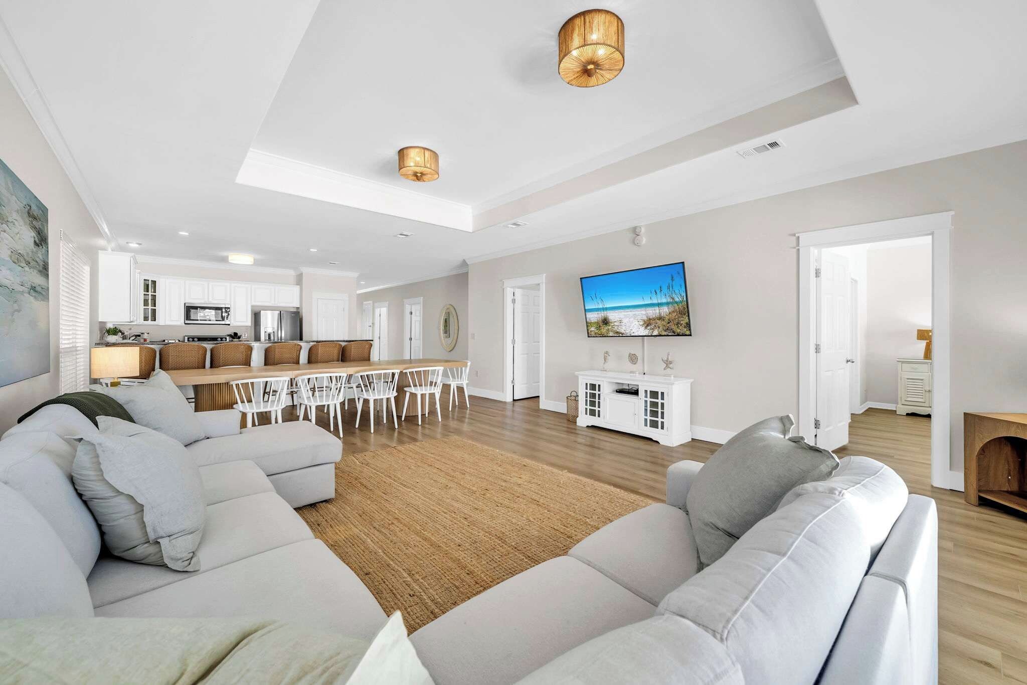 Ein modernes Wohnzimmer mit einer Eckcouch, einem Essbereich mit Tisch und Stühlen, einer Küche im Hintergrund und einem an der Wand befestigten Fernseher.