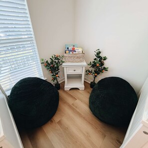 Ein Eckzimmer mit einer weißen Kommode, zwei schwarzen Sitzsäcken, einem kleinen weißen Tisch mit Büchern und zwei Kübelpflanzen mit orangen Früchten.
