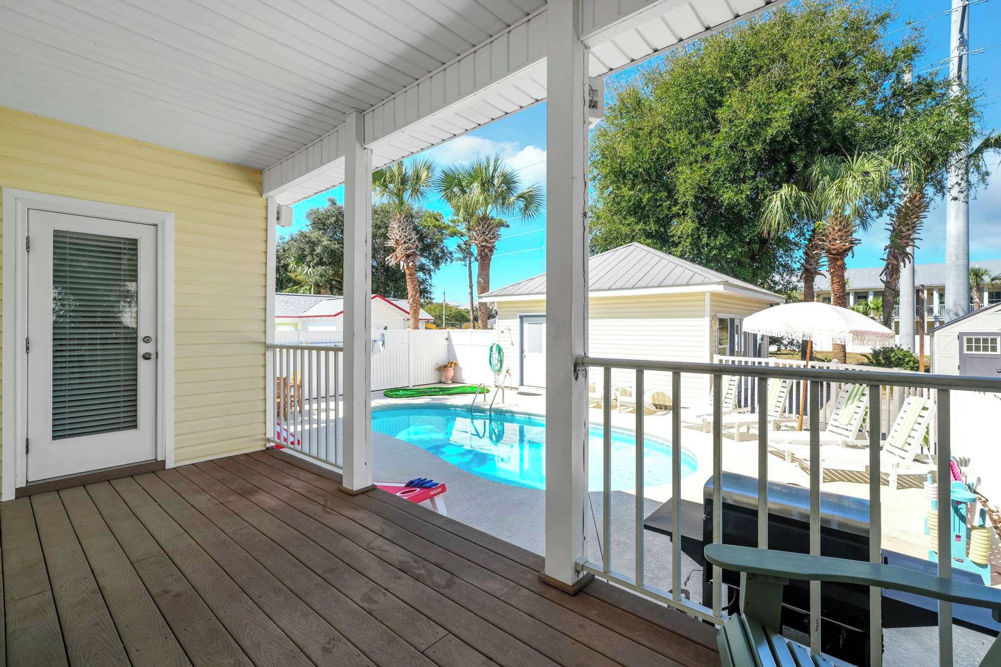 A covered wooden deck with a pool and lounge chairs.