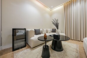 Un salon moderne avec un canapé, deux tables basses noires, un meuble vitré et une grande fenêtre avec des rideaux.