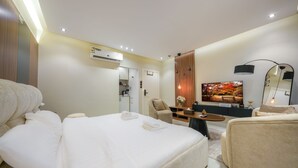 A hotel room with a bed, a desk, a chair, a TV, and an air conditioning unit. - Furnished Studio in Al-Aqiq (Riyadh)