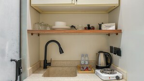 A compact kitchenette with a sink, a stove, and a shelf above the sink holding dishes and a kettle. - Furnished Studio in Al-Aqiq (Riyadh)