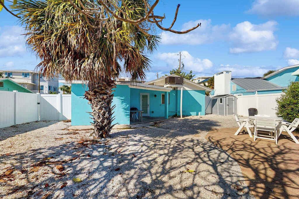Un barrio residencial con una casa azul, una palmera y un patio con sillas.
