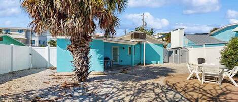 A residential area with a blue house, a palm tree, and a patio with chairs.