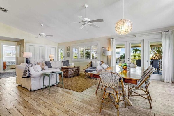 Un salón amplio con comedor, muebles blancos y ventanas grandes.