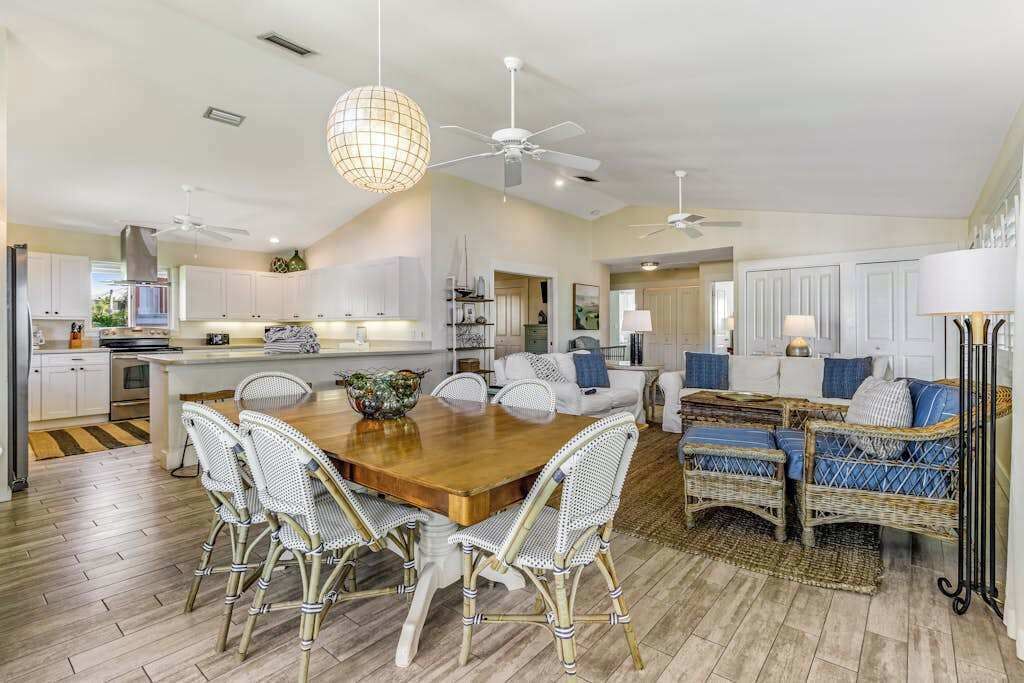A spacious kitchen with white cabinetry, a wooden dining table, wicker chairs, and ceiling fans.