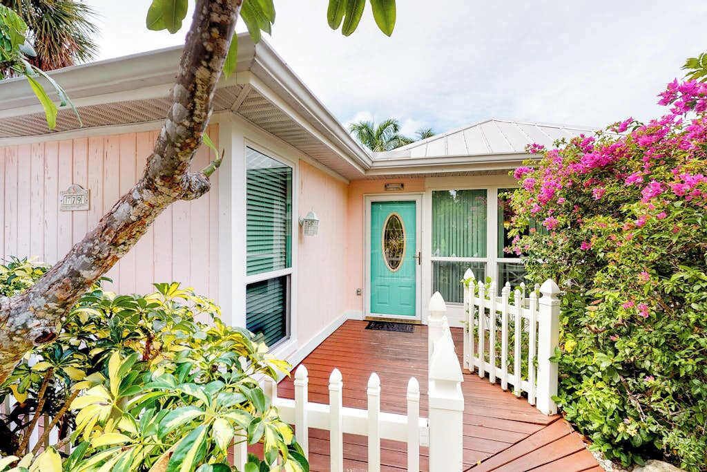 A house with a turquoise door, a white picket fence, and lush greenery.
