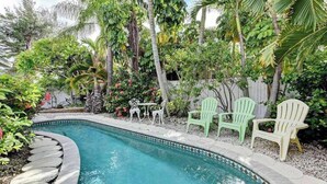 En pool med buet kant, omgivet af frodig vegetation og tre Adirondack-stole.