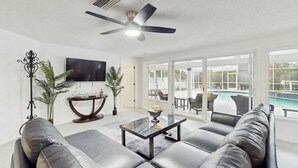 Ein modernes Wohnzimmer mit einer Couch, einem Couchtisch, einem Fernseher und einem Deckenventilator.
