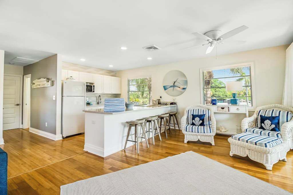 A spacious living area with a kitchen, white wicker furniture, and a ceiling fan.