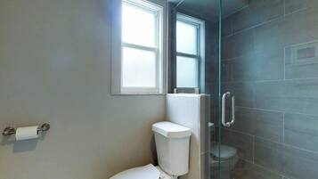 A bathroom with a toilet, a glass shower enclosure, and a window.