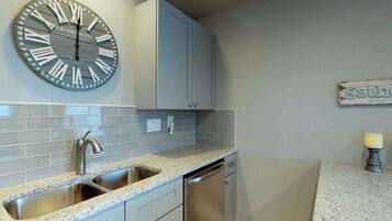 A kitchen with a sink, faucet, and dishwasher, a clock with Roman numerals, and a cabinet above the sink.
