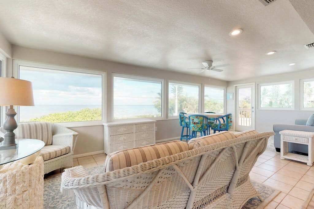 A spacious room with large windows, wicker furniture, a ceiling fan, and a view of the outdoors.