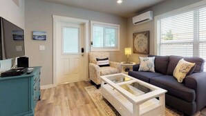 A living room with a sofa, armchair, coffee table, TV, and a dresser. - Stylish bayside condo with WiFi & pool - close to the beach & restaurants (Anna Maria)