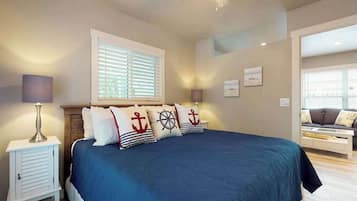 Une chambre à coucher comprenant un lit, une table de chevet, une lampe, une fenêtre avec des stores et donnant sur une autre pièce.