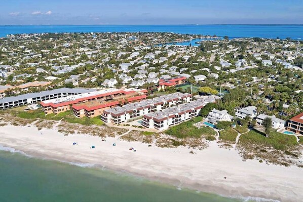 Vista aérea de una zona residencial costera con propiedades frente a la playa, incluyendo edificios de varios pisos y una playa con sombrillas.