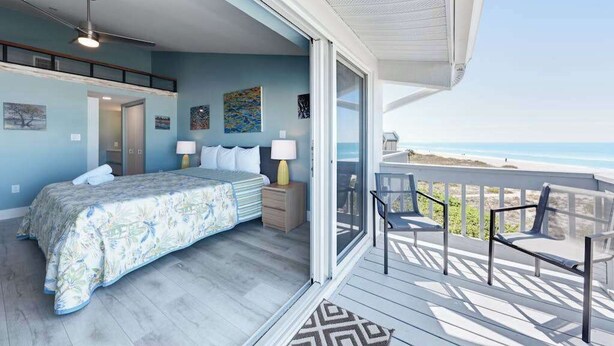 Una camera da letto con un letto, comodini e vista sulla spiaggia tramite una porta scorrevole.