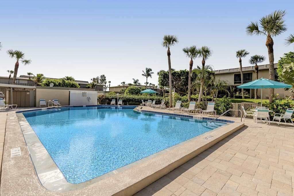A rectangular swimming pool with clear blue water, surrounded by lounge chairs and palm trees.