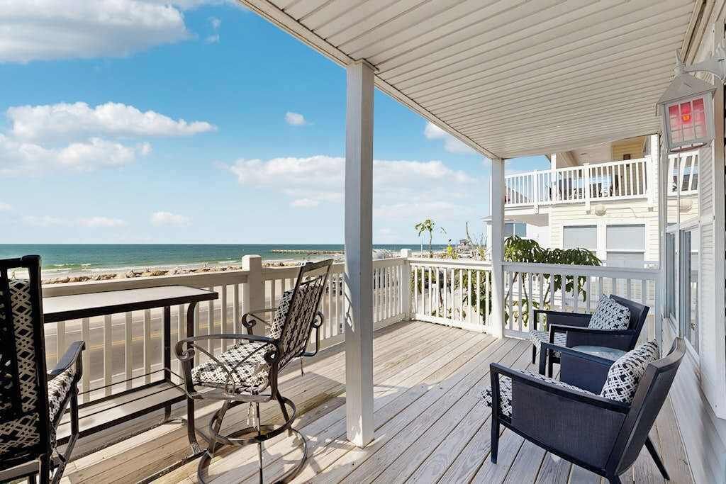 A covered balcony with a view of the beach, furnished with chairs and a table.