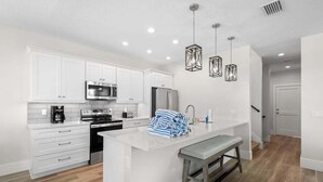 Una cocina moderna con muebles blancos, electrodomésticos de acero inoxidable y una isla central con taburetes.