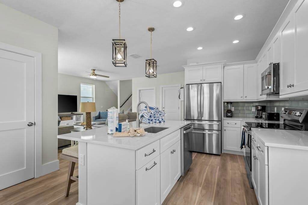 A modern kitchen with white cabinetry, stainless steel appliances, and pendant lighting.