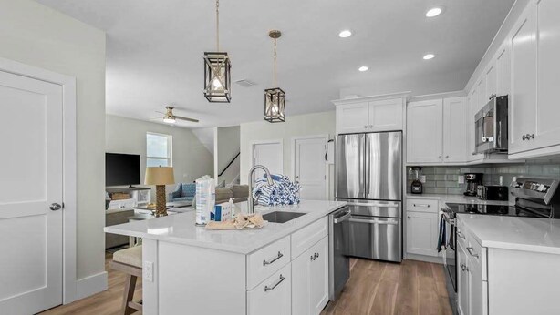 Une cuisine moderne avec des meubles blancs, des appareils en acier inoxydable et des luminaires suspendus.