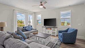 Un salon avec un canapé gris, une table basse, un téléviseur posé sur un meuble et un ventilateur de plafond.