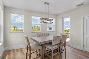Une salle à manger avec une table et des chaises en bois, de grandes fenêtres et un luminaire suspendu.