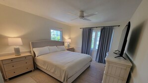 Ein Schlafzimmer mit einem Bett, Nachttischen, einem Fernseher, einem Deckenventilator und einem Fenster mit Vorhängen.