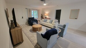 Ein Wohnzimmer mit einer Couch, Sesseln, einem Couchtisch und einem Fernseher auf einem Lowboard.