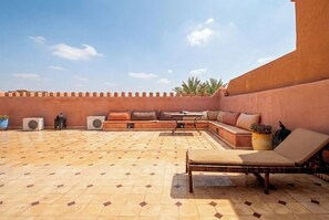 Un espace extérieur aménagé avec un petit muret, un banc rembourré, un fauteuil confortable et un sol carrelé.