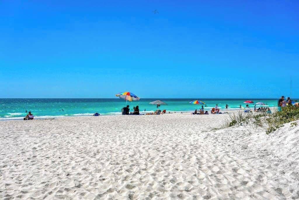 Une plage de sable blanc, avec une eau d’un bleu limpide et des parasols.