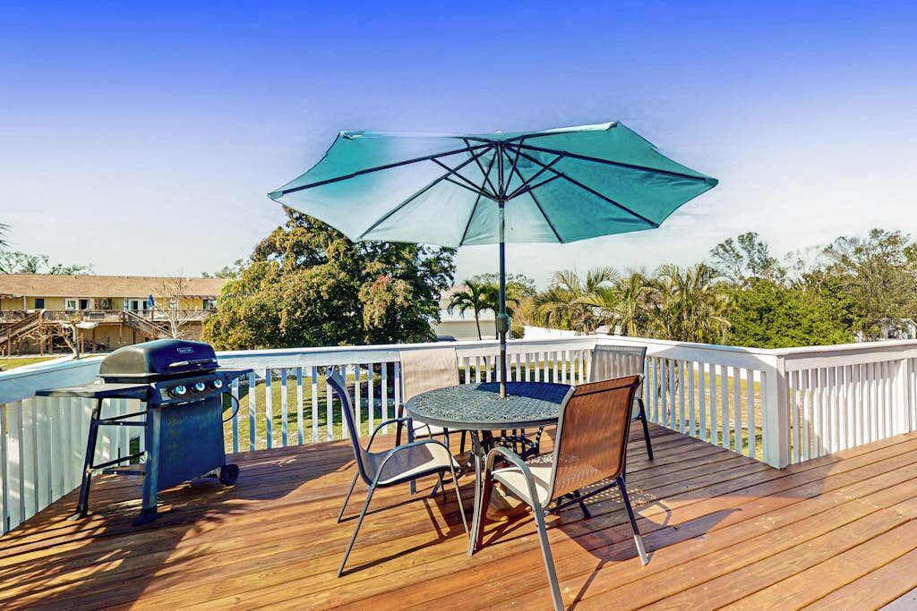Une terrasse en bois avec un barbecue, une table et des chaises, ainsi qu’un parasol.