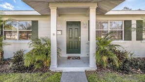 Una casa de un piso con puerta verde, revestimiento blanco y porche cubierto.