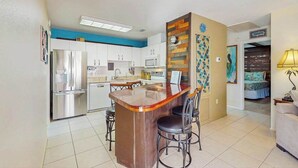 Een moderne keuken met een centraal eiland, witte kasten, roestvrijstalen apparatuur en een blauwe accentmuur.