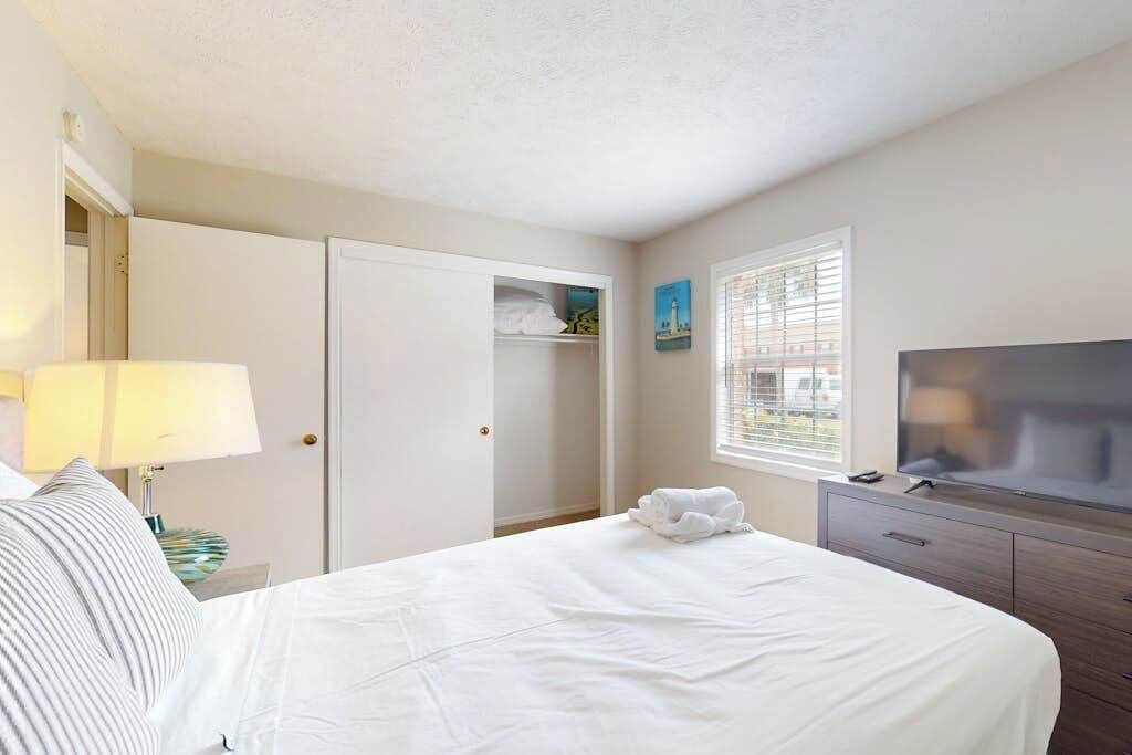 A hotel room with a bed, a TV, a wardrobe, and a window with blinds.