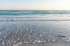 Ein Strand mit sanften Wellen, blauem Himmel und einem Stock im Sand.