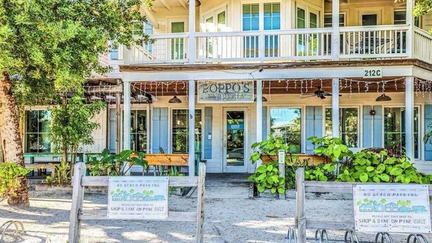 Un edificio a due piani con un portico, indicazioni per il parcheggio in spiaggia e un ristorante chiamato 'Poppo's Bar & Restaurant' all'indirizzo '212C'.