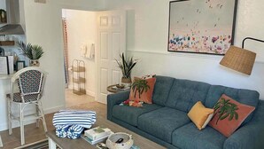 Una sala de estar con un sofá, una silla, una mesa baja con libros y una cesta, y un cuadro en la pared.