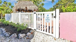 Zona vallada con una estructura de techo de paja, una cerca blanca y un cartel que indica acceso solo para huéspedes registrados.